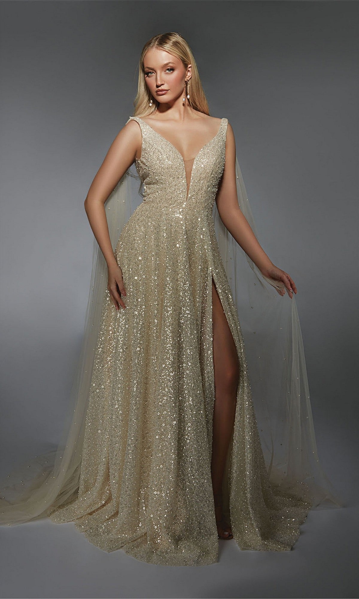A woman stands gracefully against a plain gray background wearing the Alyce 7134—a sleeveless, floor-length white gown with a deep V-neckline and high slit.